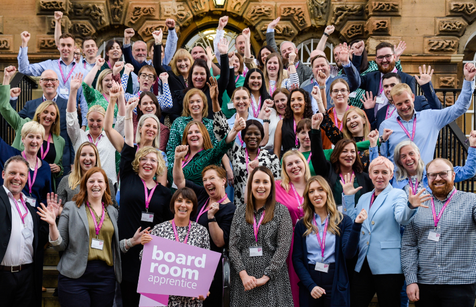 large group of boardroom apprentices standing on outdoor steps raise their arms and cheer