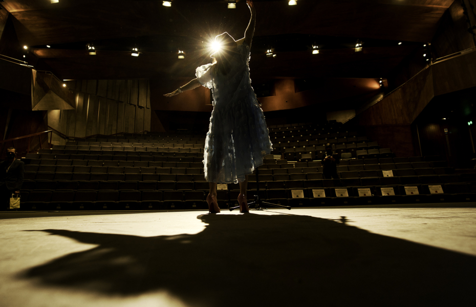 A silhouette figure is on stage, with an empty theatre in front of them