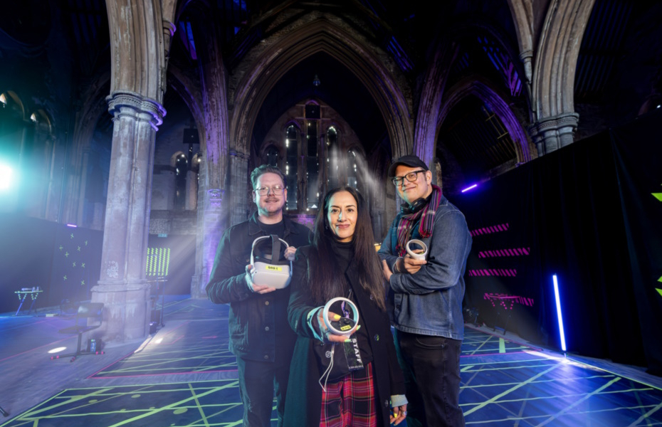 Three people standing in a church holding VR headsets in their hands and looking towards the camera.