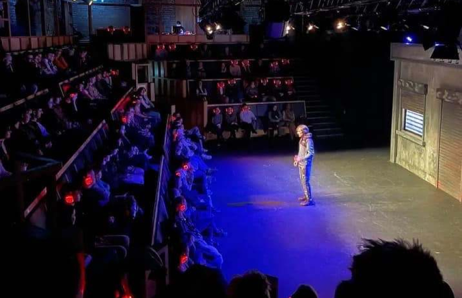 Man on a theatre stage, performing to a crowd.