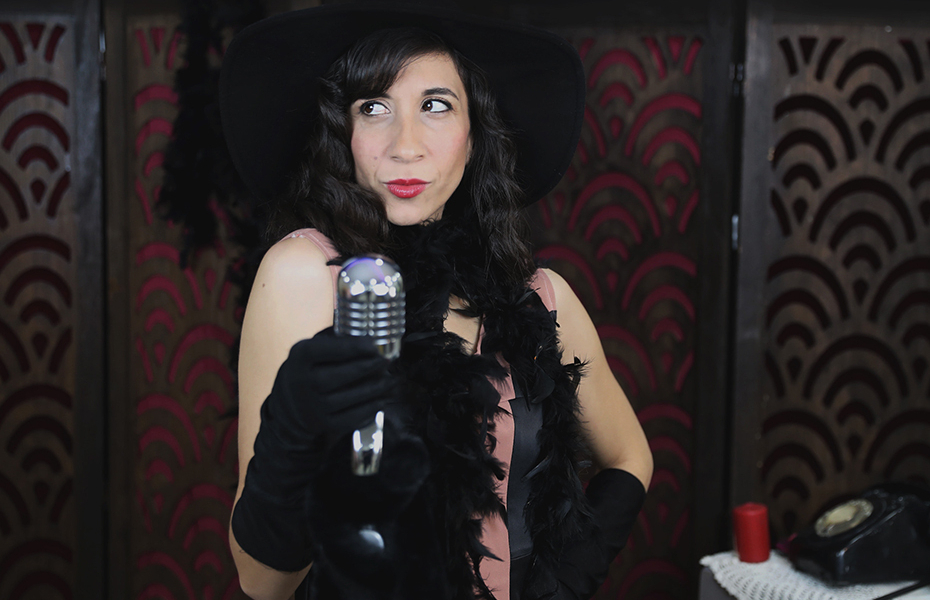 Female singer wearing a black dress, black hat and a black feather boa.