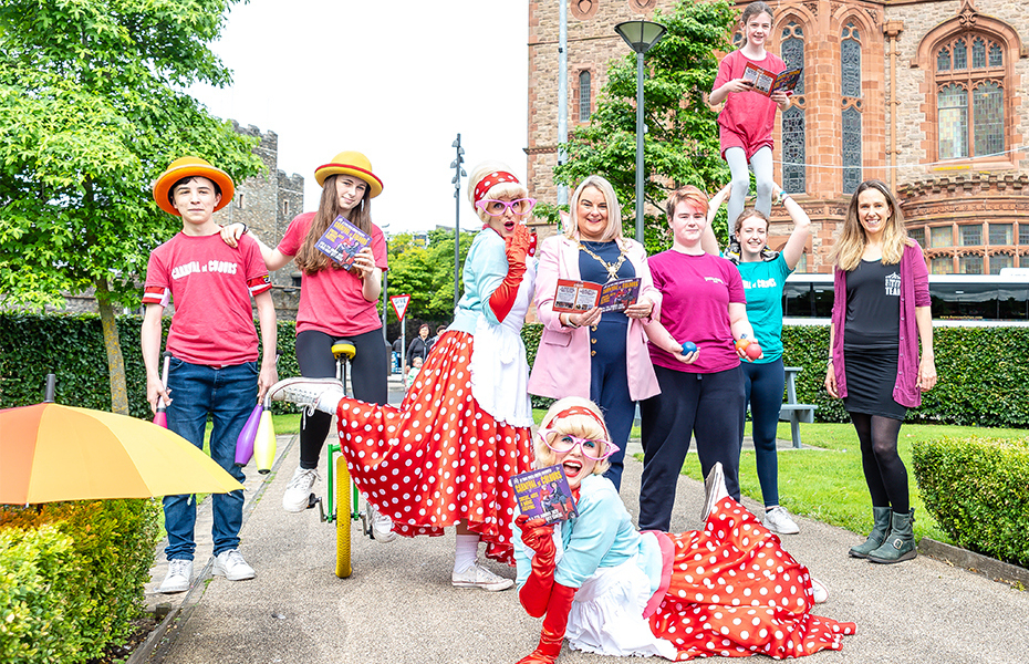 Group of street performers outside the Guildhall in Derry-Londonderry with three females holding the programme for the 2022 Carnival of Colours.