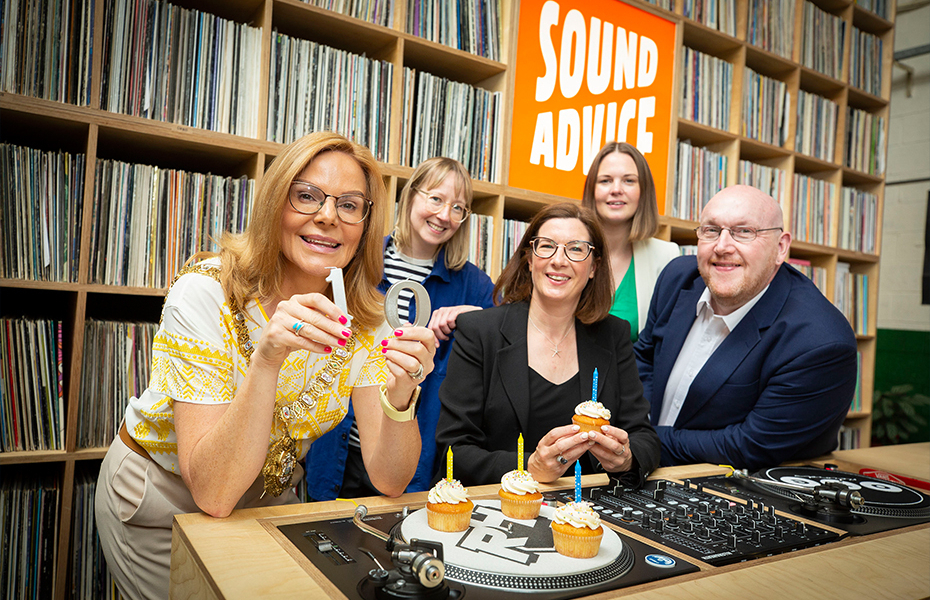 Four females and one male stood beside Dj Decks holding cupcakes with candles and a wall of music records in the background.