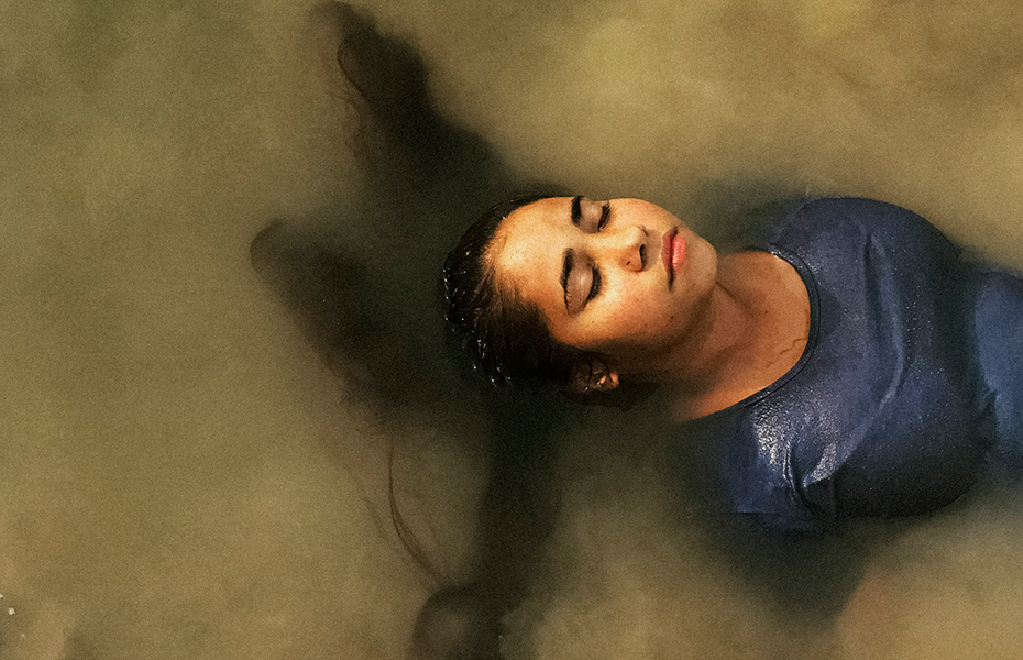 Female with long dark hair and a blue top partially submerged in cloudy water.